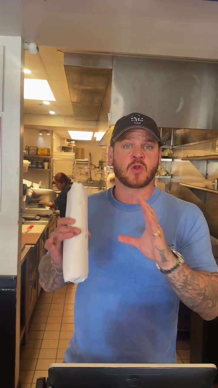 The owner of Uncle Paulie's behind the counter, a wrapped sandwich in his hand